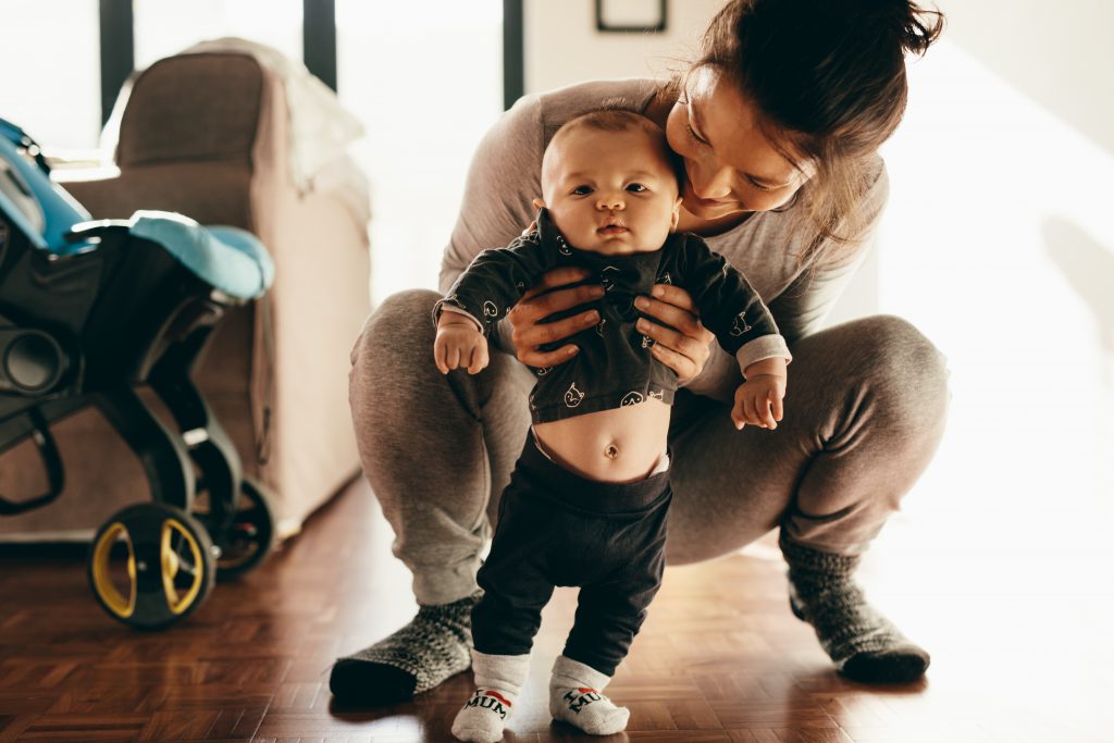 A woman plays with her baby, squatting on the floor and holding him