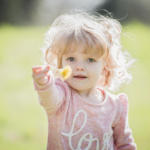 A young girl hands a flower toward the camera
