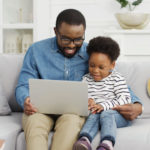 A father and daughter look at a laptop together