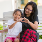 A mom and daughter use their hands to make a heart