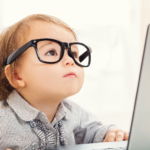 A young child wearing over-sized glasses looks at a laptop