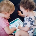 Two toddlers look at a tablet