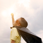 A child dressed as a superhero holds his fist up to the sky