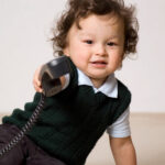 A toddler holds a landline phone